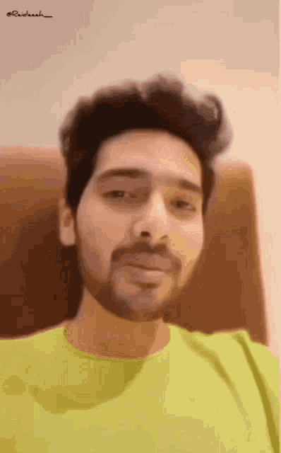a man with a beard wearing a green shirt is sitting in a chair .