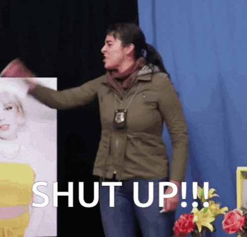 a woman in a green jacket is standing in front of a sign that says " shut up "