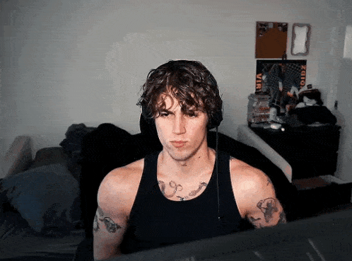 a man with tattoos is wearing headphones and looking at a computer screen .