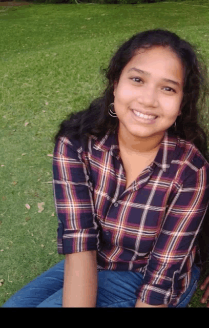 a woman in a plaid shirt sits in the grass and smiles