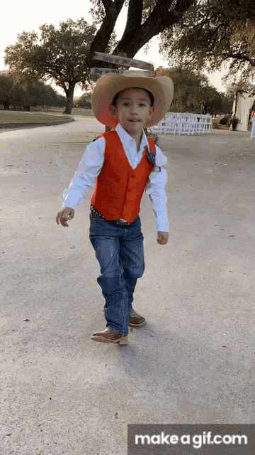 a young boy wearing a cowboy hat and vest is walking down a street