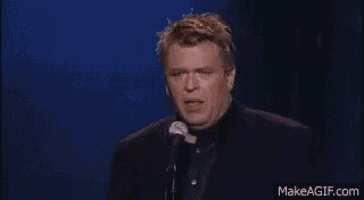 a man in a suit is holding a glass of whiskey in front of a microphone .