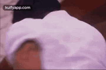a man in a white shirt is laying on a bed with his head down .