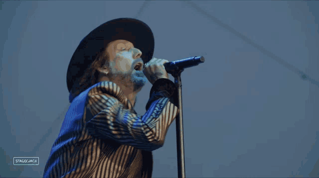 a man in a blue hat is standing in front of a microphone with the words stage mica visible in the corner