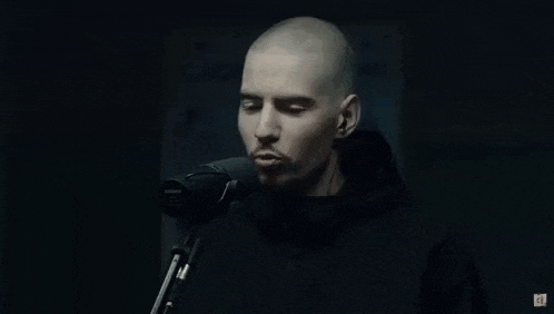 a bald man is singing into a microphone in front of a poster .