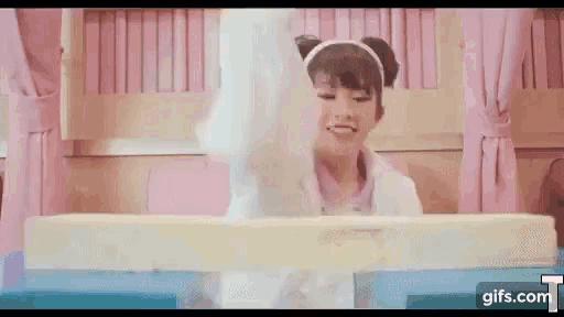 a girl is sitting in a bed with a pink curtain and a white blanket on her head .