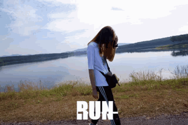 a woman walking in front of a lake with the word run written on the ground