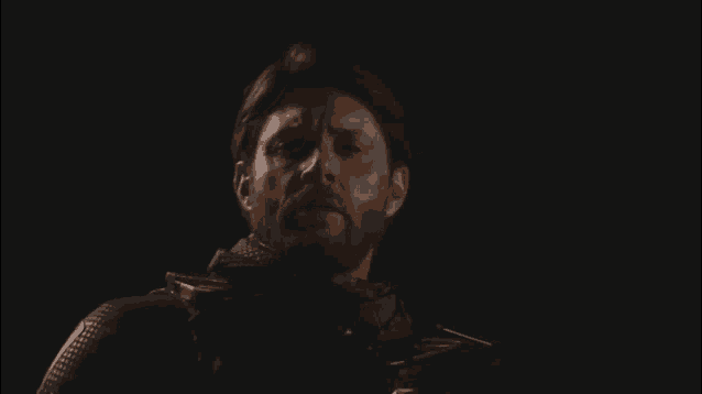 a man with a beard is standing in the dark with his eyes closed .