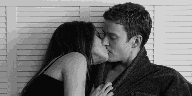 a man and woman kissing in front of a white wall