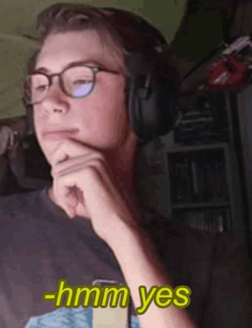 a young man wearing glasses and headphones says " hmm yes " in yellow letters