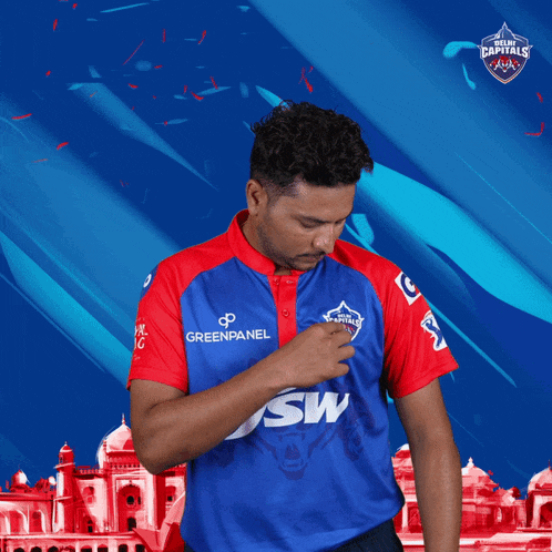 a man wearing a delhi capitals jersey stands in front of a building