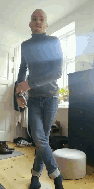 a man wearing a turtleneck and jeans is dancing in a living room .