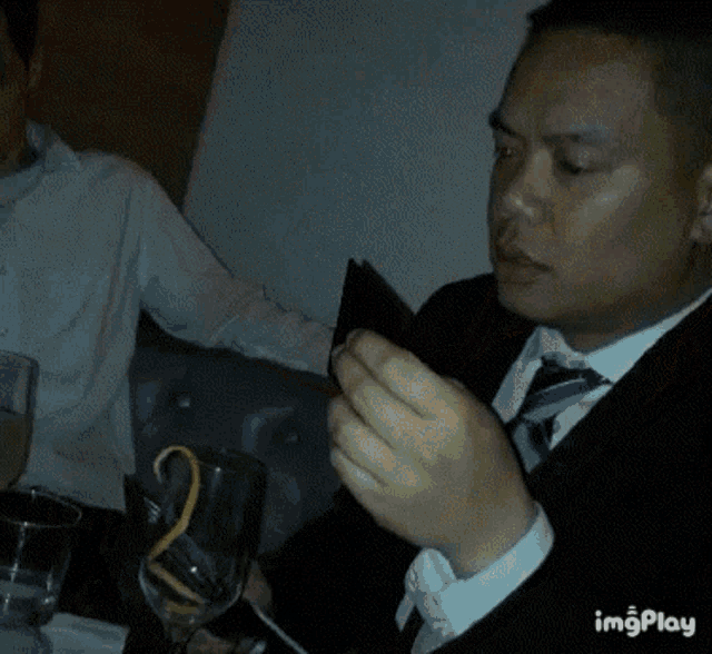 a man in a suit and tie is sitting at a table with a glass of wine and a cell phone .