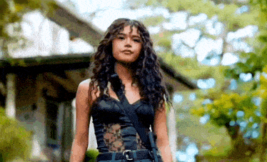 a woman with curly hair is standing in front of a house wearing a black top .
