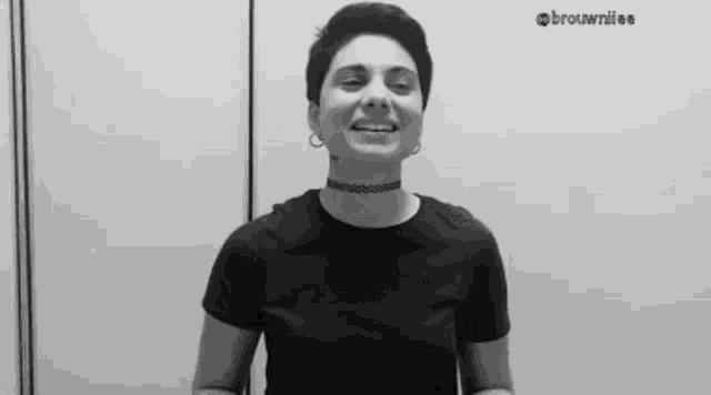 a black and white photo of a woman wearing a choker and a black shirt smiling .