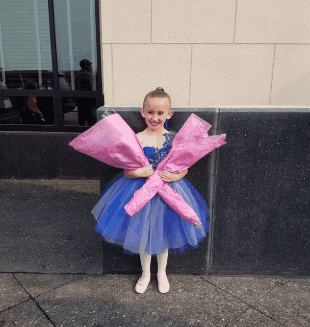a little girl in a blue dress is holding flowers