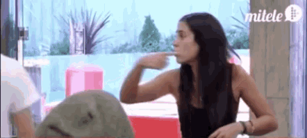 a woman in a black tank top is sitting at a table with a man and pointing at him .