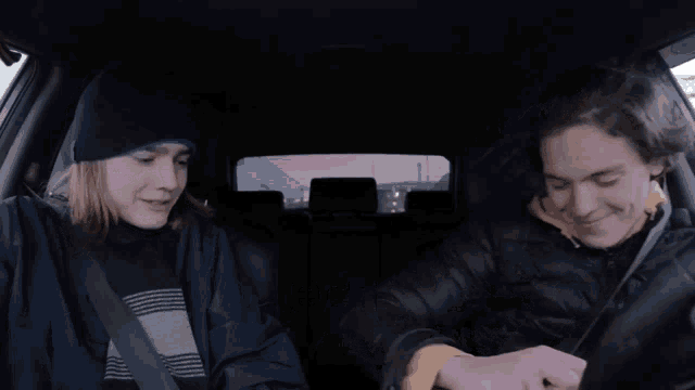 two young men are sitting in a car and one of them is wearing a beanie and the other is wearing a jacket
