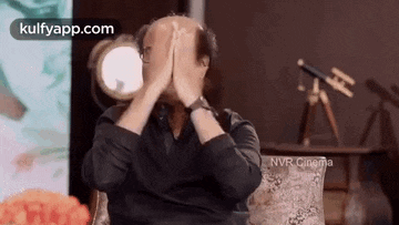 a man is covering his face with his hands while sitting on a couch .