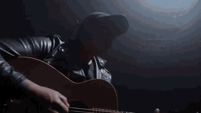 a man in a leather jacket is playing an acoustic guitar