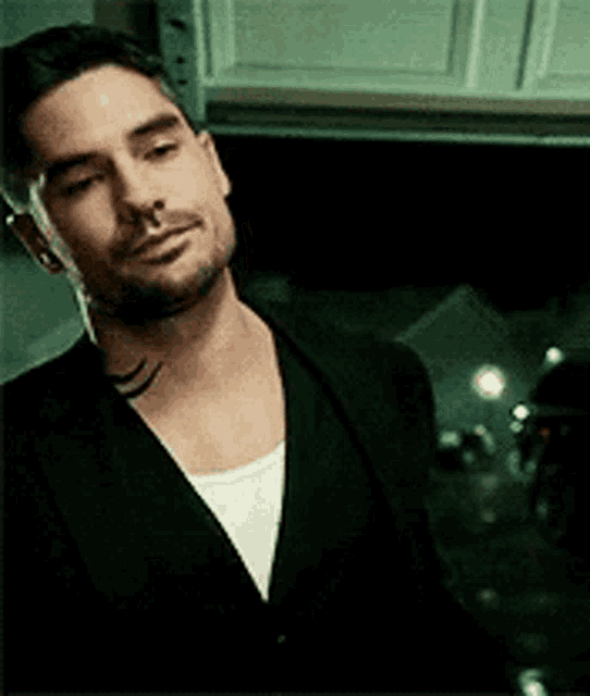 a man with a tattoo on his neck is wearing a black jacket and white shirt .