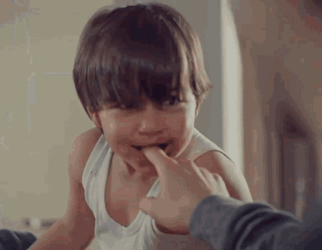 a young boy in a white tank top bites his finger