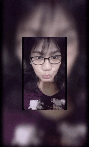 a woman wearing glasses and a purple shirt looks at the camera