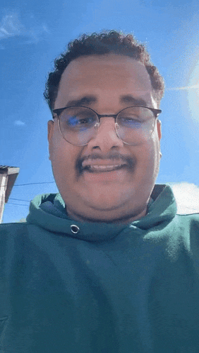 a man wearing glasses and a green hoodie smiles