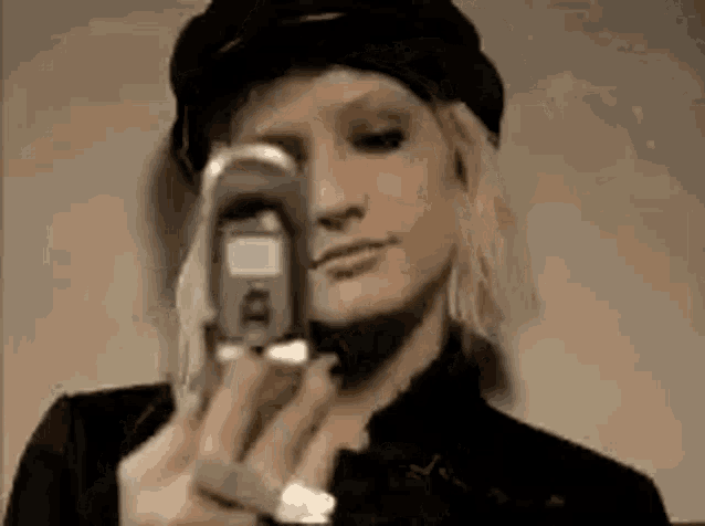 a woman wearing a hat is taking a picture of herself with a cell phone .