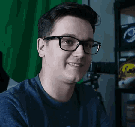 a young man wearing glasses and a blue shirt is smiling .