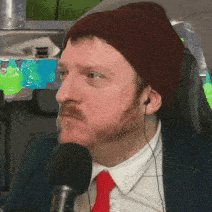 a man with a beard wearing a beanie and ear buds is talking into a microphone