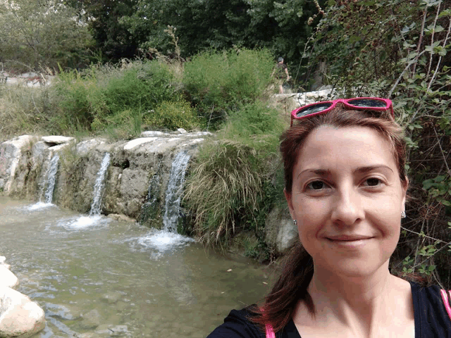 a woman wearing pink sunglasses is standing in front of a waterfall