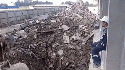 a man wearing a hard hat is sitting in front of a pile of rubble