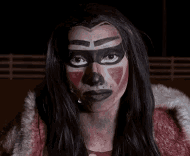 a woman with blood on her face is wearing a scary mask .