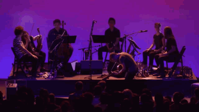 a group of people playing instruments on a stage with purple lights