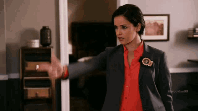 a woman in a suit and red shirt is standing in front of a door .