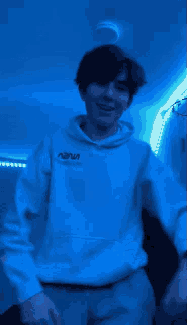 a young man wearing a nasa hoodie is standing in a room with blue lights