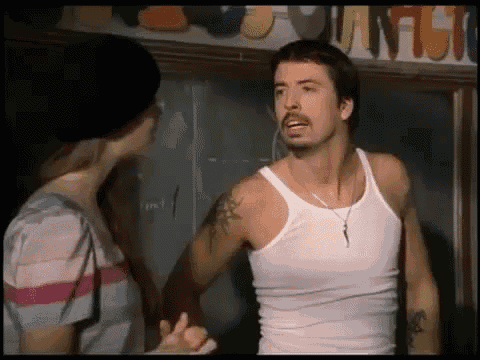 a man in a white tank top is standing next to a woman in a classroom .