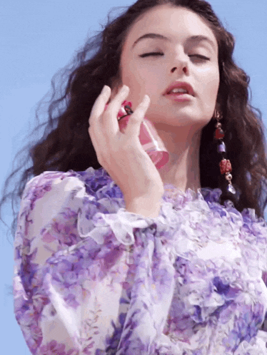 a woman in a purple floral dress is spraying perfume on herself