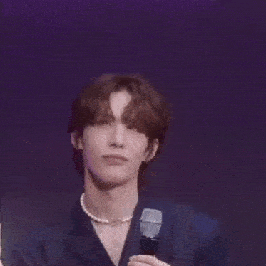 a man wearing a pearl necklace and a suit is holding a microphone in his hand .