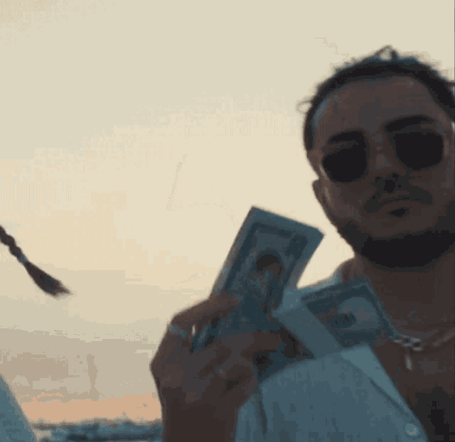 a man wearing sunglasses holds a stack of money