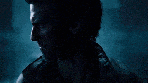 a man with a beard is standing in a dark room with red and blue lights behind him .