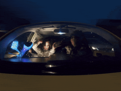 two women are sitting in a car at night looking at their cell phones