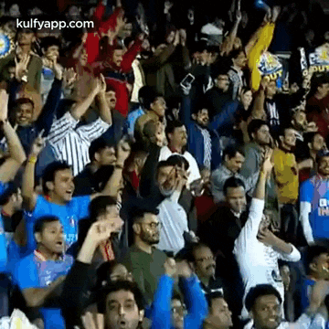 a crowd of people are standing in a stadium watching a game and cheering .