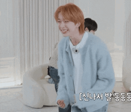 a young man with red hair is wearing a blue sweater and smiling while sitting on a couch .