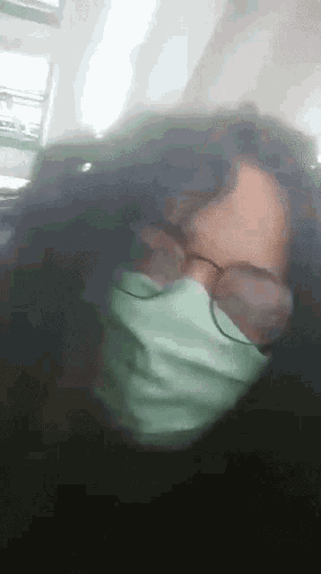 a woman wearing glasses and a green mask looks at the camera