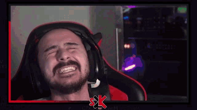 a man with a beard is wearing headphones and making a funny face while sitting in a gaming chair .