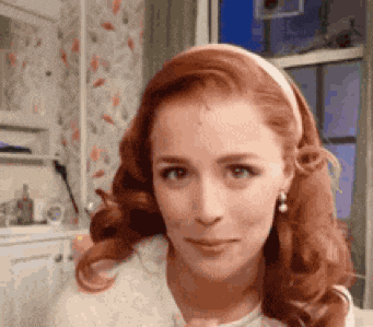 a woman with red hair is wearing a headband and earrings and looking at the camera .