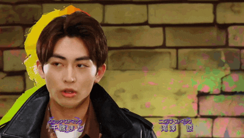 a man in a black leather jacket stands in front of a brick wall with chinese writing on it