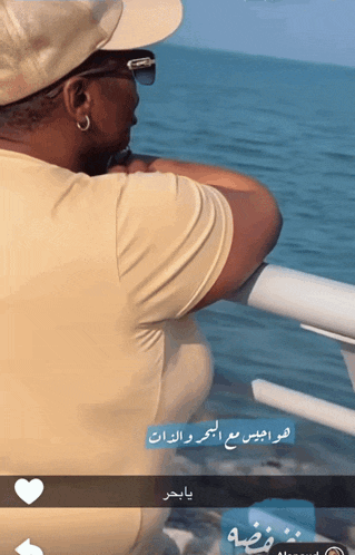 a man wearing a hat and sunglasses is looking out over the ocean